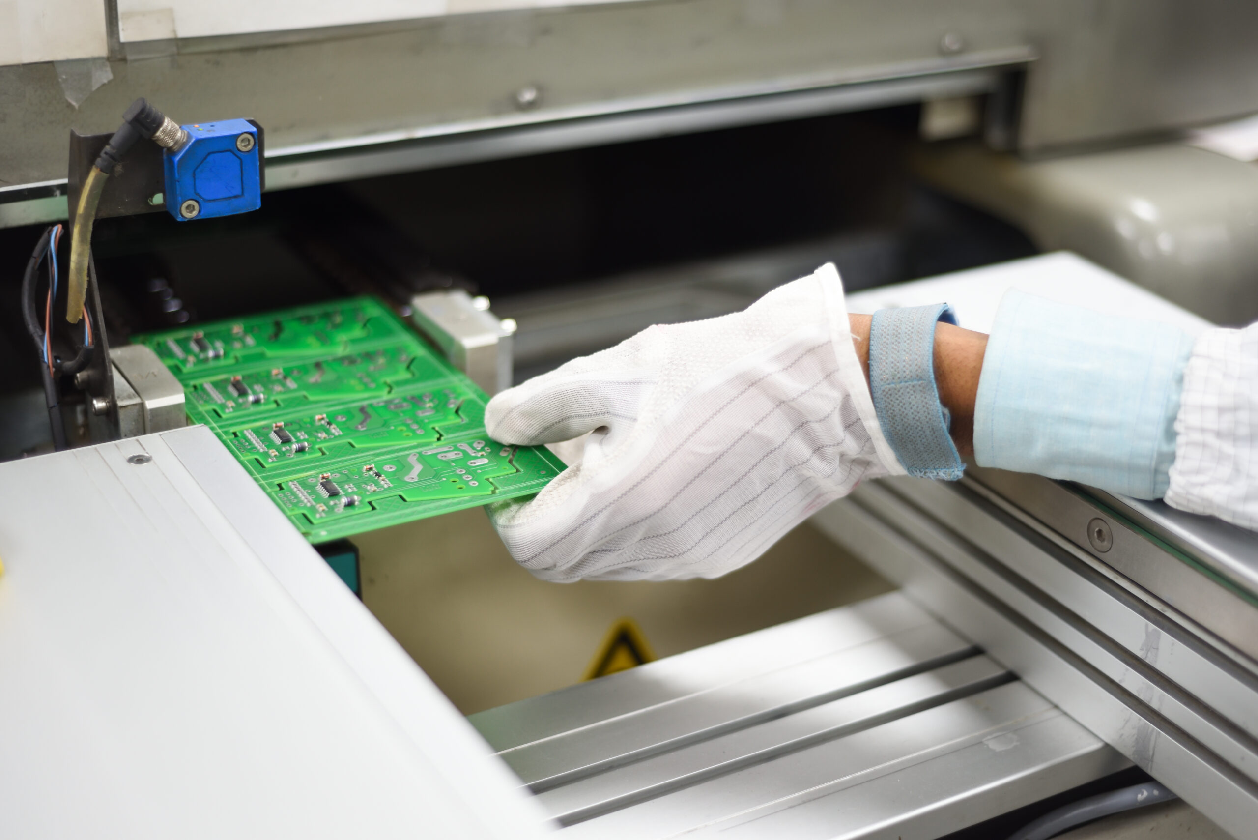 Electronic manufacturing factory workers hand covered with ESD gears removing printing circuit board from SMT line